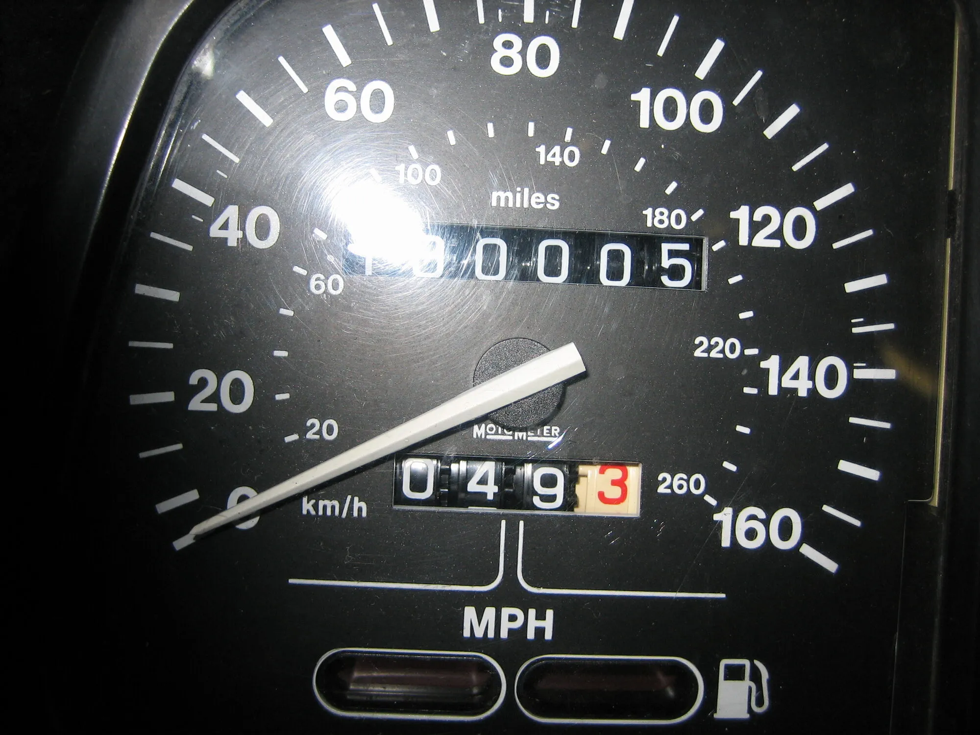 Motorcycle odometer reading 100,005 miles under a dash light